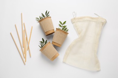 Photo of Paper cups with green twigs, mesh bag and bamboo straws on white background, flat lay. Eco friendly lifestyle