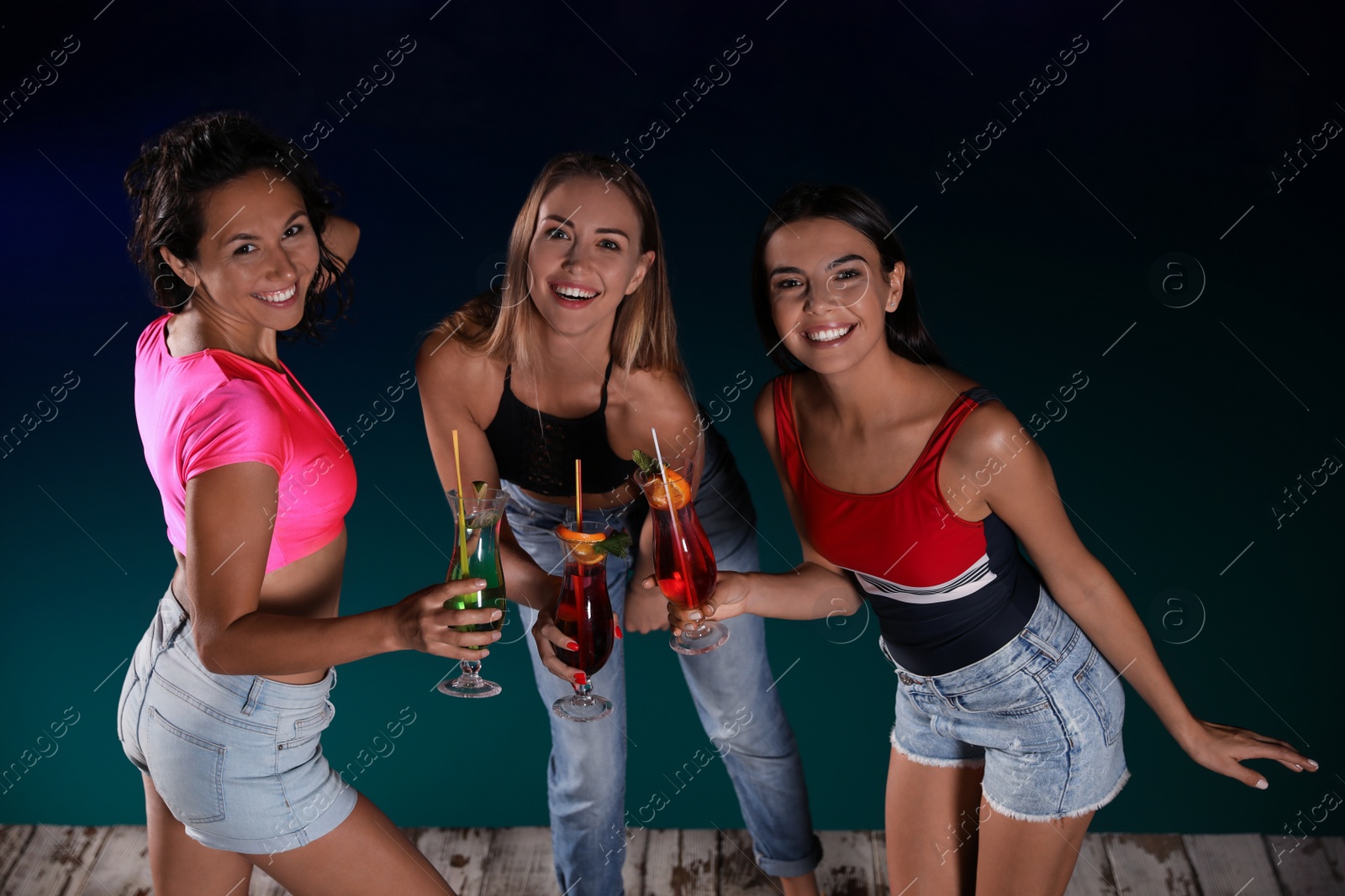 Photo of Happy young friends with refreshing cocktails relaxing near outdoor swimming pool at night