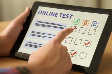 Man taking online test on tablet at desk indoors, closeup