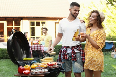 Photo of Young man and woman with drinks near barbecue grill outdoors