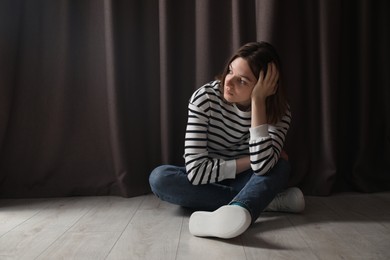 Sad young woman sitting on floor indoors, space for text