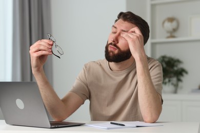 Overwhelmed man sitting with laptop at table indoors