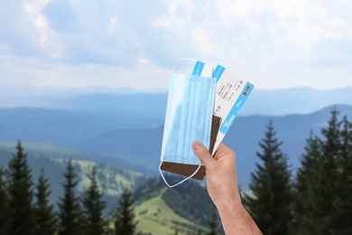 Image of Man holding passport, tickets and protective mask outdoors, closeup. Travel during quarantine