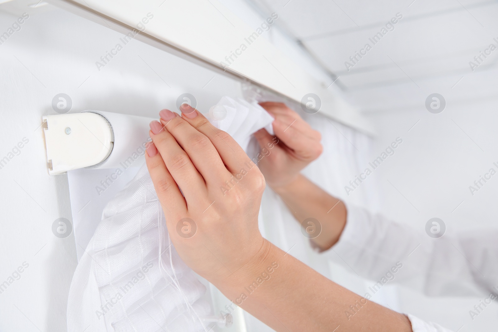 Photo of Woman hanging window curtain indoors, closeup. Interior decor element