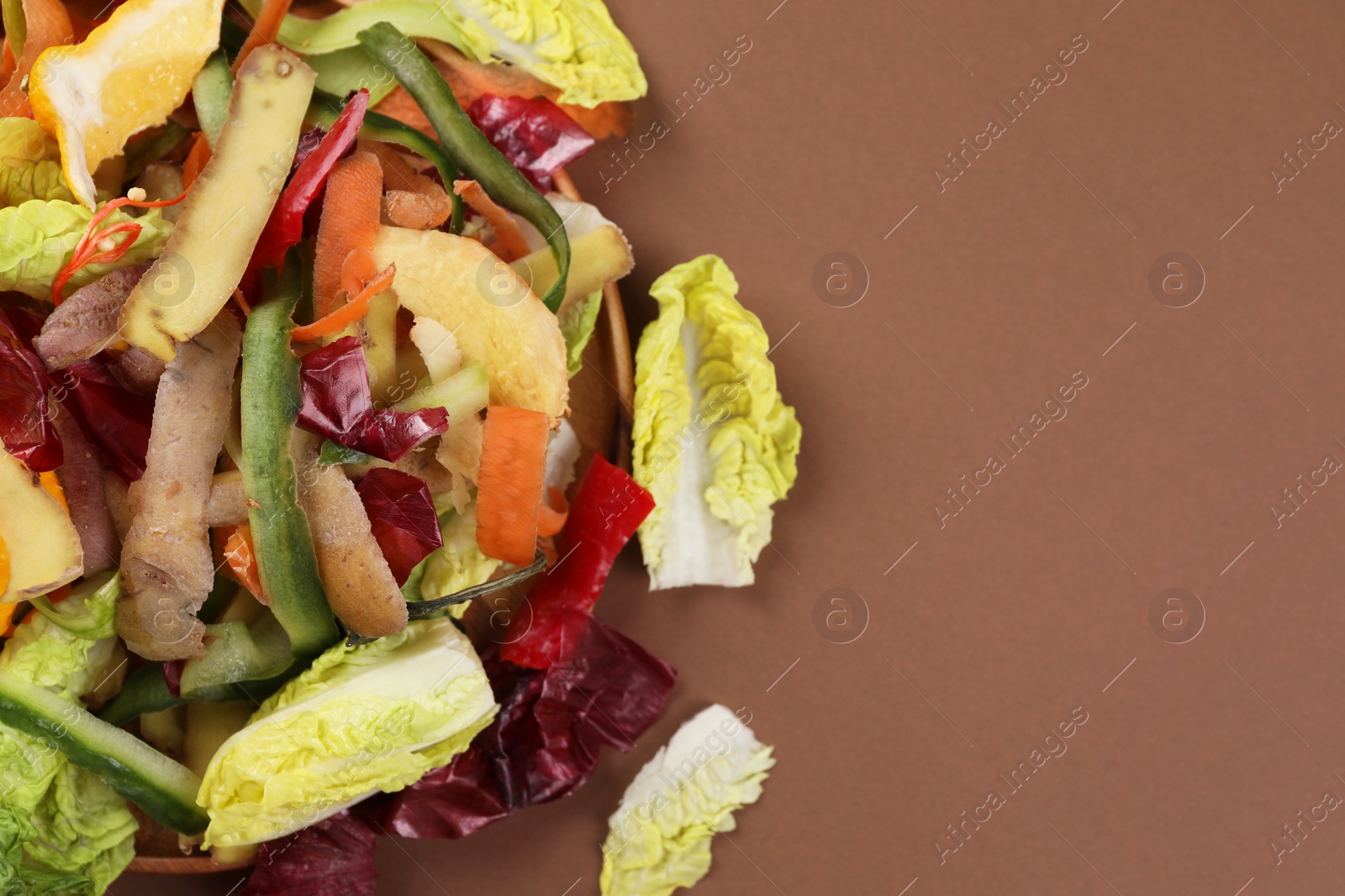 Photo of Peels of fresh vegetables on brown background, top view. Space for text