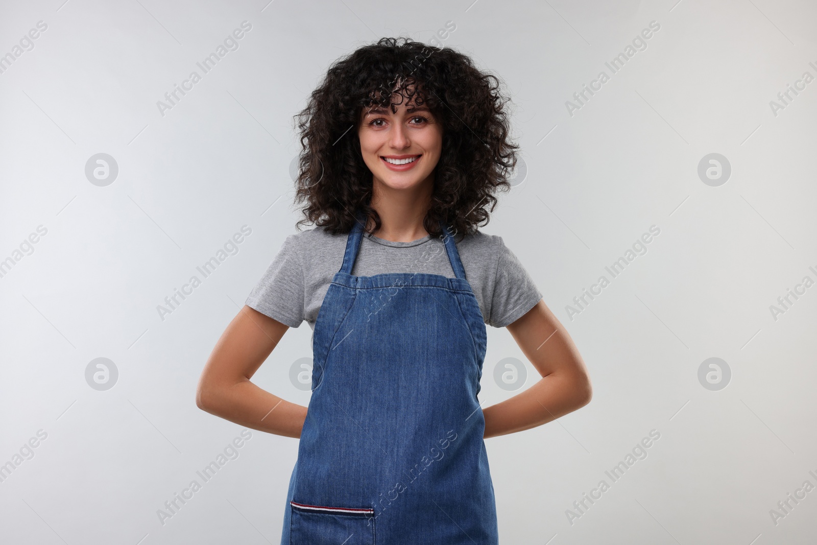 Photo of Happy woman wearing kitchen apron on light grey background. Mockup for design