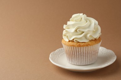 Photo of Tasty vanilla cupcake with cream on dark beige background, space for text