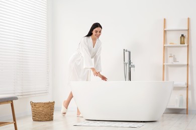 Photo of Beautiful happy woman wearing stylish bathrobe near tub in bathroom