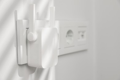 Wireless Wi-Fi repeater on white wall indoors, space for text