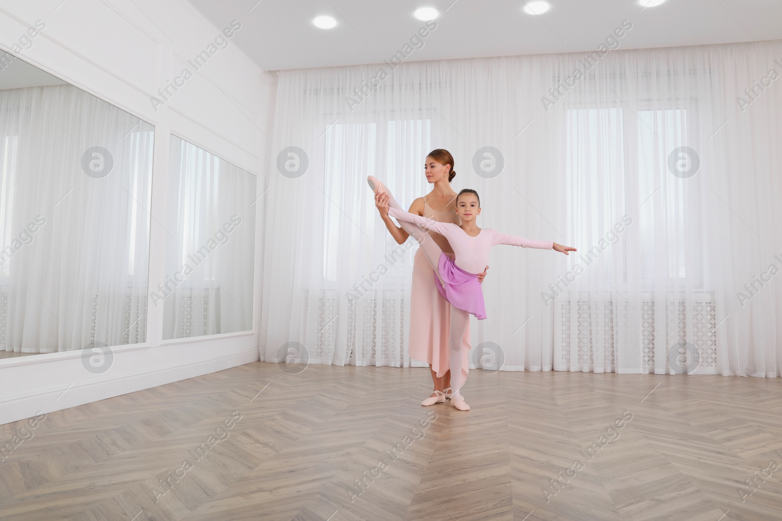 Photo of Little ballerina and her teacher practicing dance moves in studio