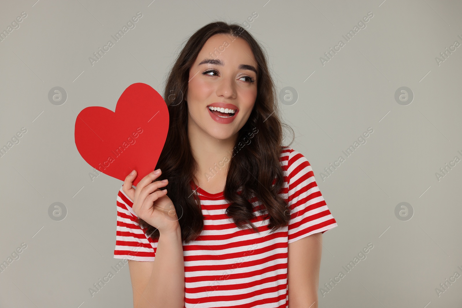 Photo of Beautiful young woman with paper heart on grey background