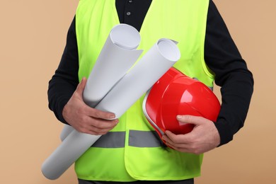 Architect with hard hat and drafts on beige background, closeup