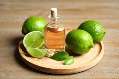 Photo of Lime essential oil and citrus fruits on wooden table