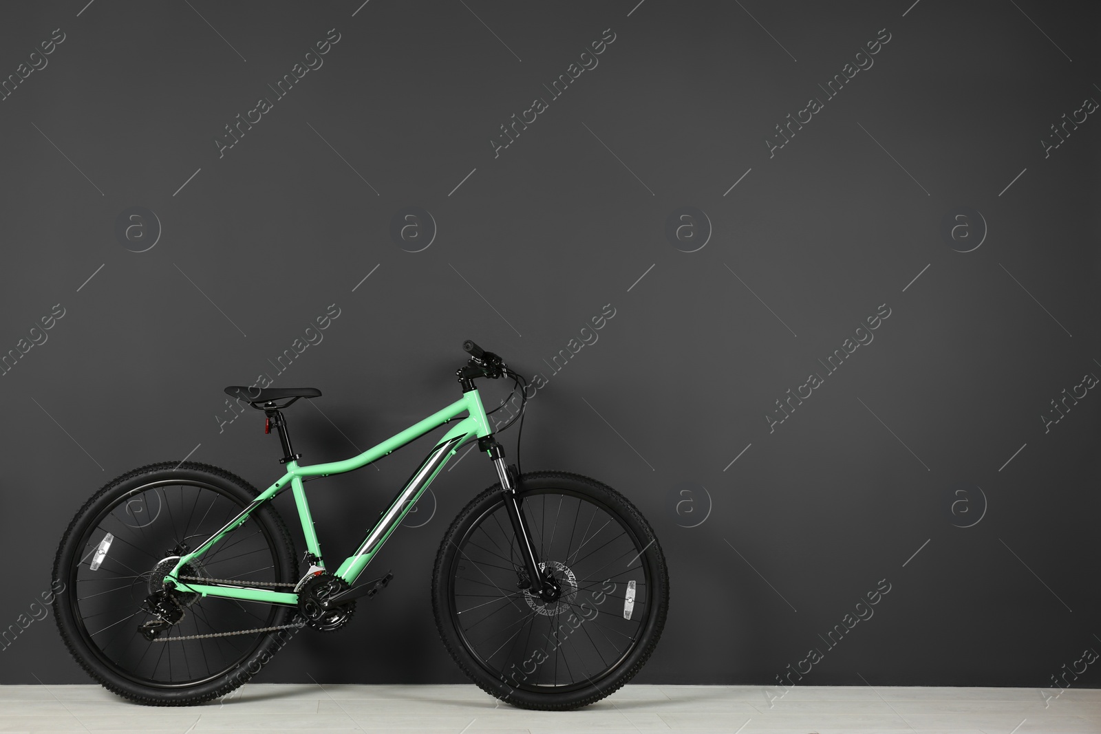 Photo of Modern bicycle near dark wall indoors. Space for text
