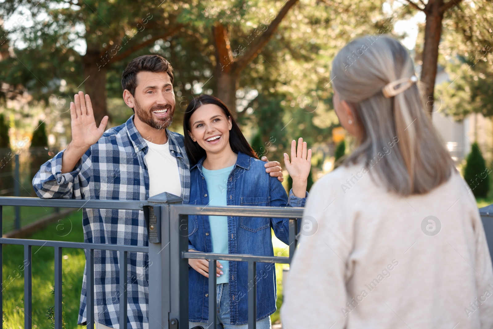 Photo of Friendly relationship with neighbours. Happy young couple greeting senior woman near fence outdoors