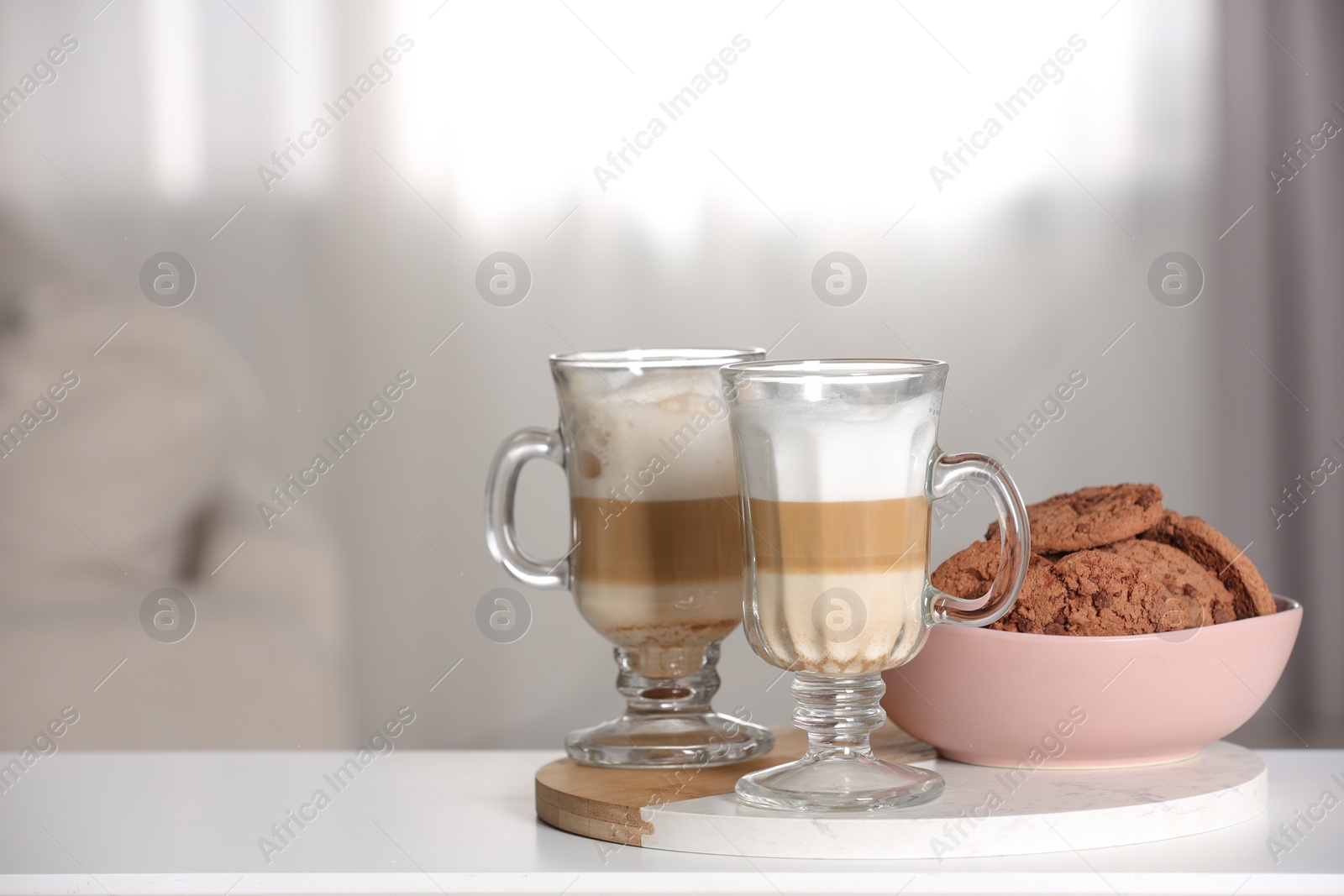 Photo of Aromatic latte macchiato in glasses and chocolate cookies on white table against light background. Space for text