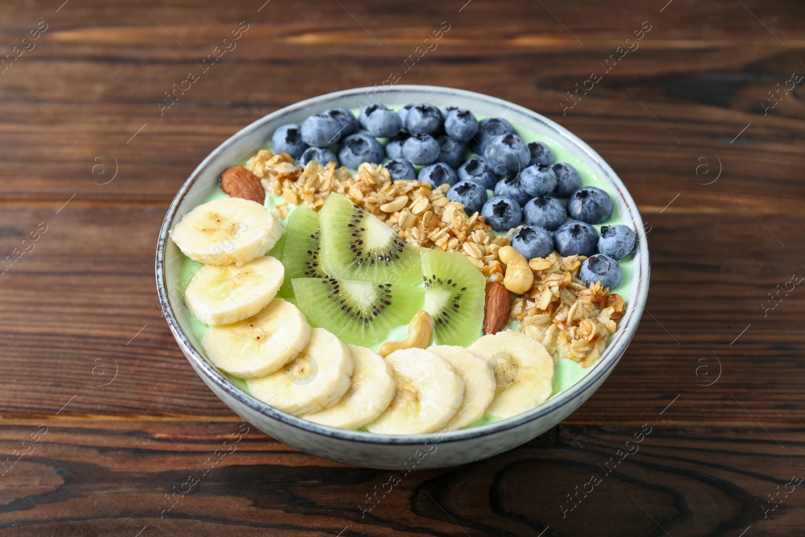 Photo of Tasty smoothie bowl with fresh fruits and oatmeal on wooden table