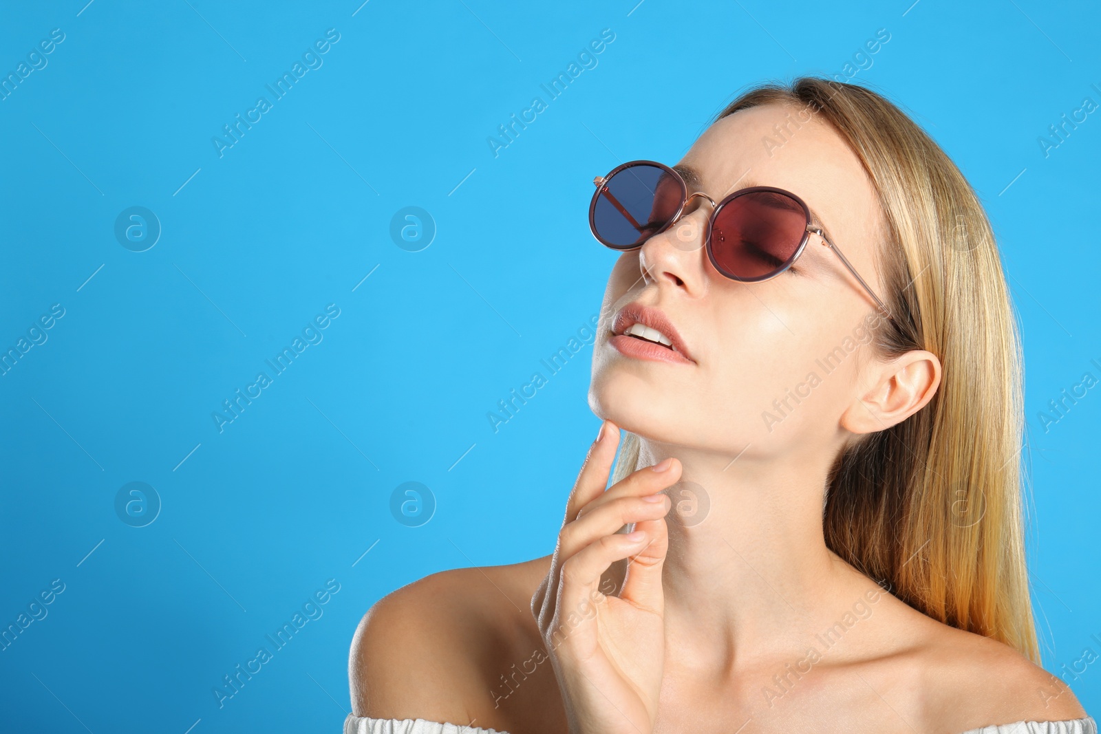 Photo of Beautiful woman in stylish sunglasses on light blue background. Space for text