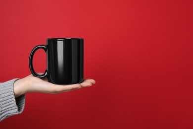 Photo of Woman holding black mug on red background, closeup. Space for text