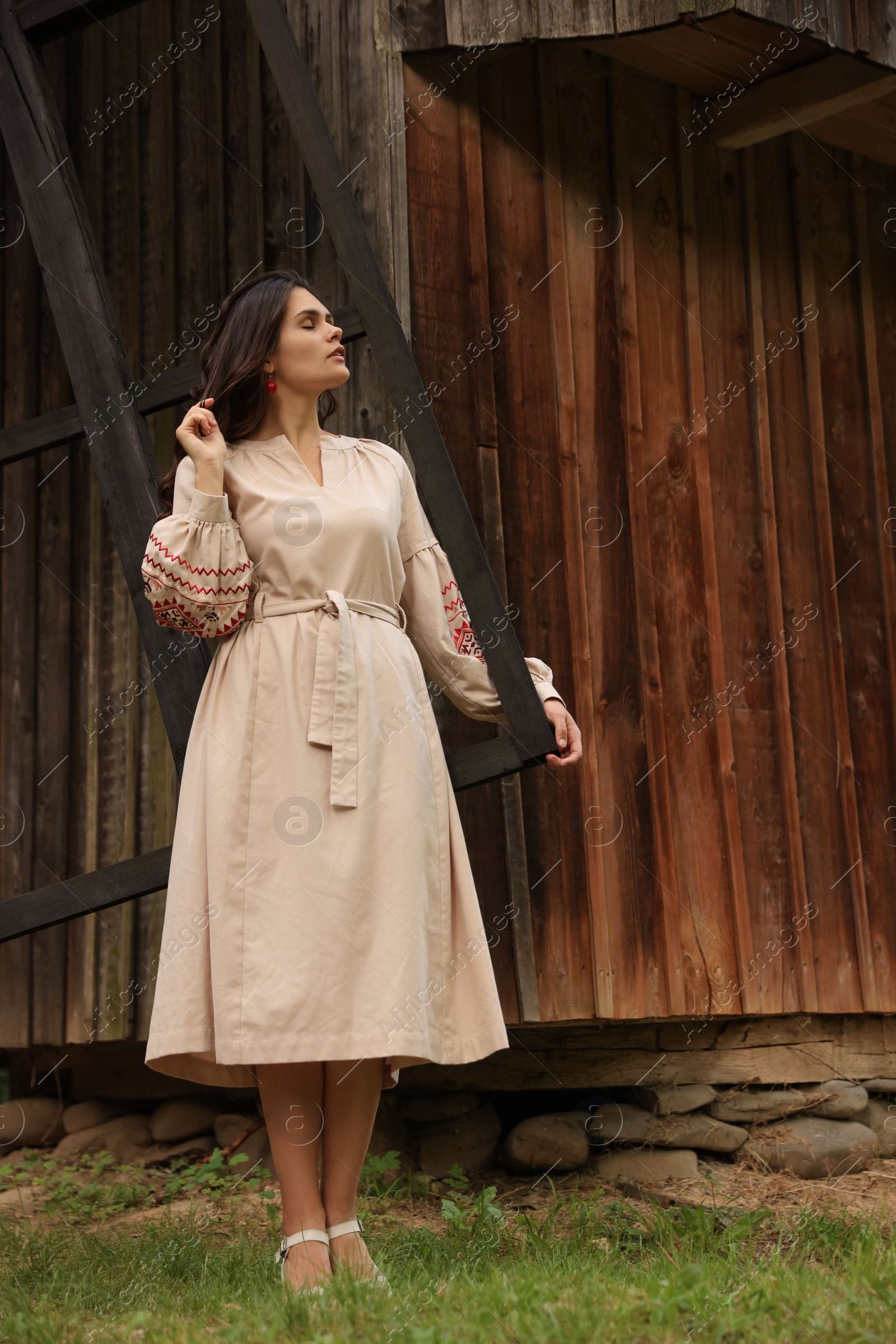 Photo of Beautiful woman wearing embroidered dress near old wooden mill in countryside. Ukrainian national clothes