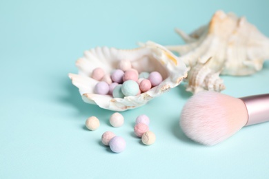 Photo of Powder balls, make up brush and sea shell on light blue background, closeup