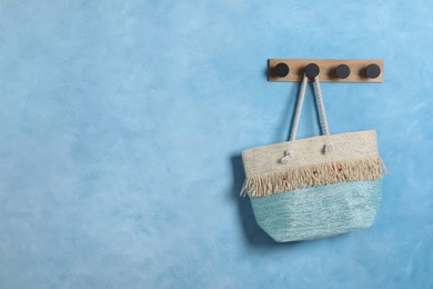 Stylish beach bag hanging on wooden rack near light blue wall, space for text