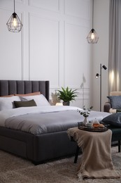 Photo of Stylish bedroom interior with large comfortable bed and ottoman