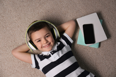 Photo of Cute little boy listening to audiobook on floor, top view