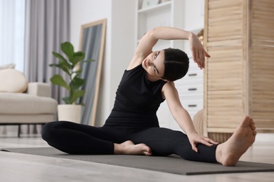 Photo of Girl practicing revolved head to knee asana on yoga mat at home. Parivrtta janu sirsasana pose