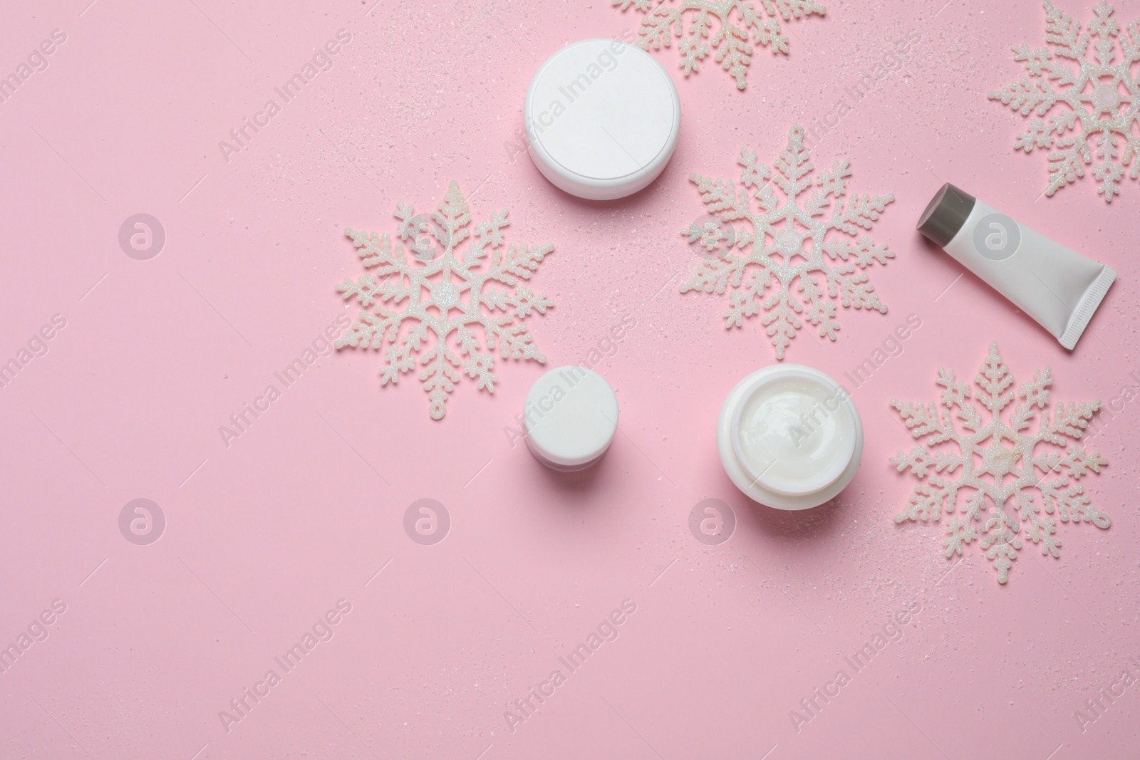 Photo of Flat lay composition with cosmetic products and snowflakes on pink background, space for text. Winter skin care