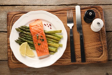 Photo of Tasty grilled salmon served with asparagus and lemon on wooden table, top view