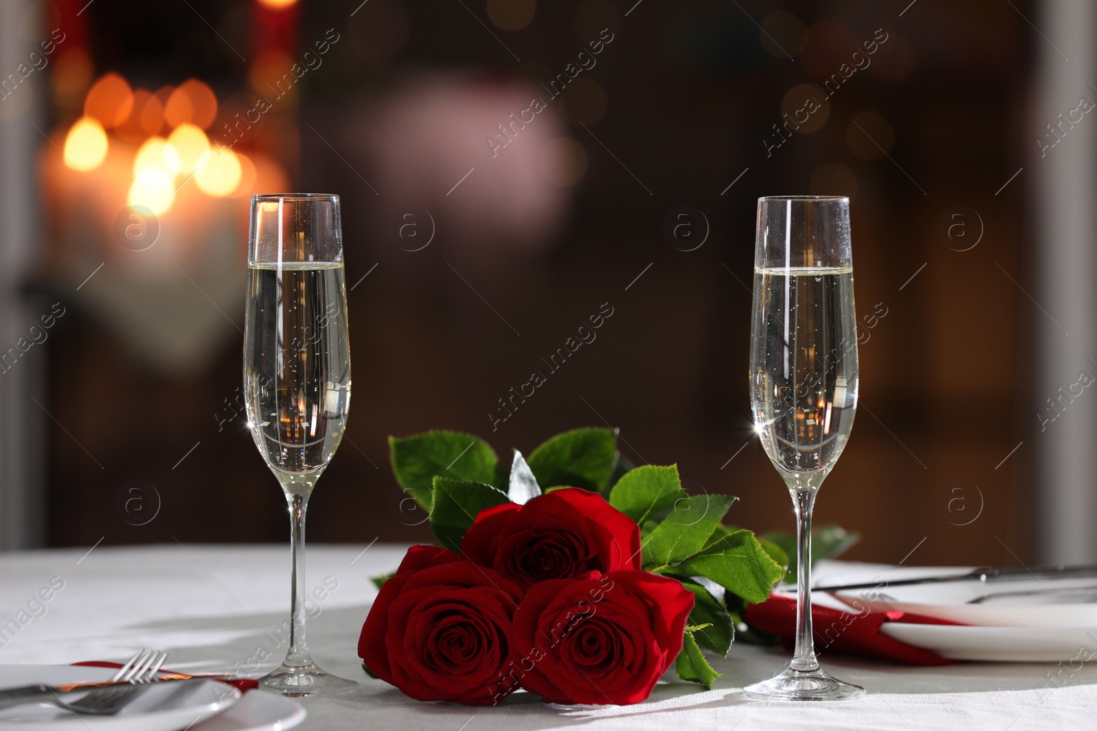 Photo of Romantic dinner table setting with glasses of champagne and red roses in restaurant