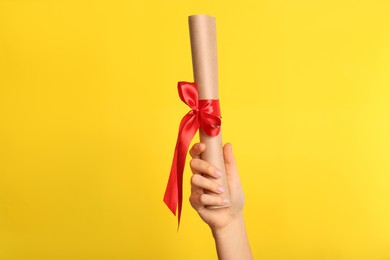 Photo of Student holding rolled diploma with red ribbon on yellow background, closeup