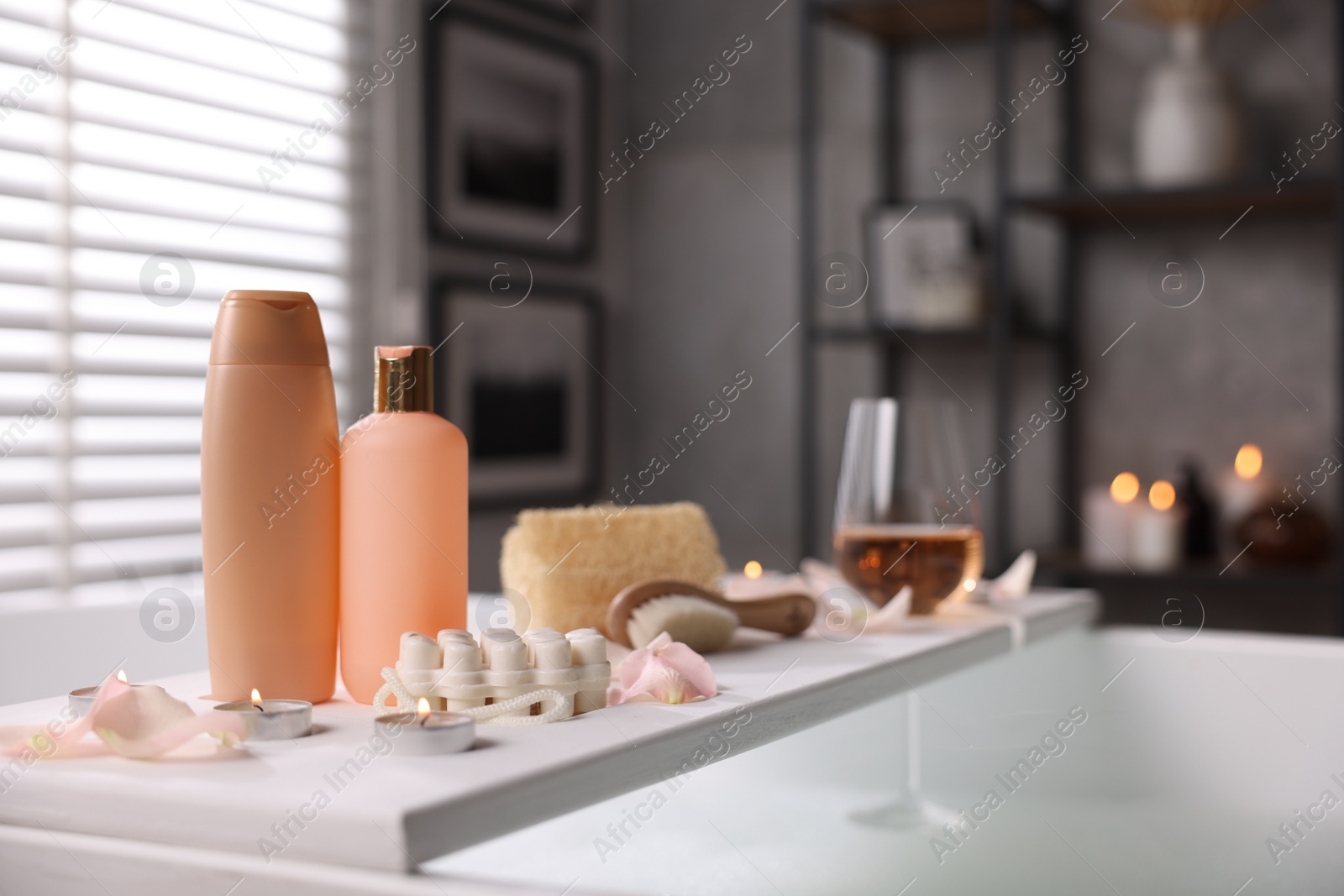 Photo of Wooden tray with wine, toiletries and flower petals on bathtub in bathroom