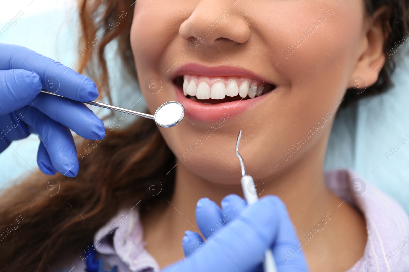 Photo of Dentist examining African-American woman's teeth with probe and mirror, closeup