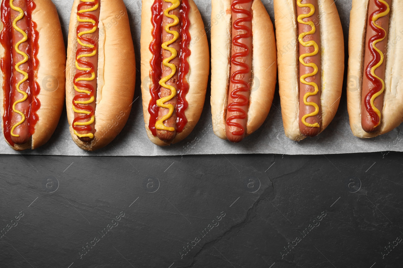 Photo of Fresh delicious hot dogs with sauces on black table, top view. Space for text