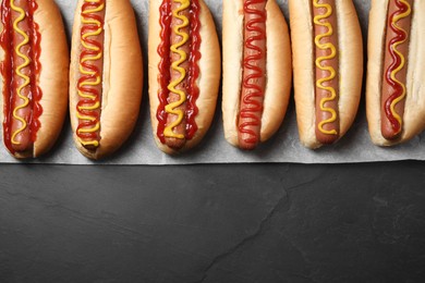 Fresh delicious hot dogs with sauces on black table, top view. Space for text