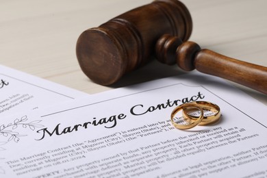 Photo of Marriage contracts, gold rings and gavel on light wooden table, closeup