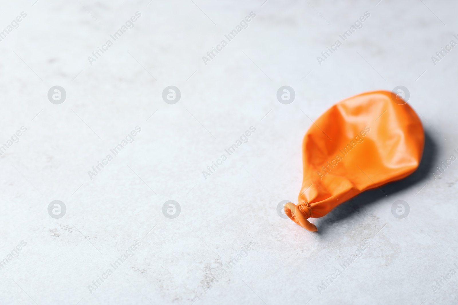 Photo of Orange deflated balloon on grey background, space for text