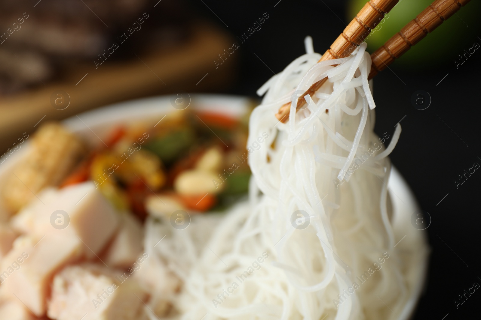 Photo of Chopsticks with tasty cooked rice noodles over bowl, closeup. Space for text