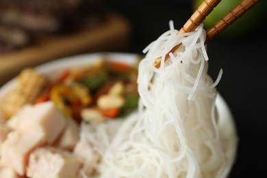 Photo of Chopsticks with tasty cooked rice noodles over bowl, closeup. Space for text