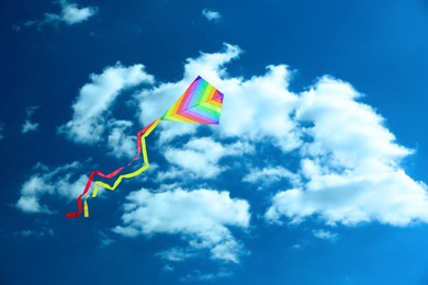 Image of Bright striped rainbow kite flying in blue sky on sunny day