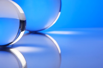 Photo of Transparent glass balls on mirror surface against blue background, closeup
