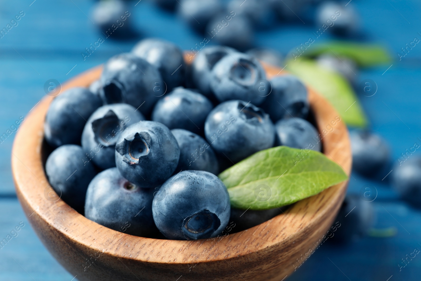 Photo of Bowl of fresh tasty blueberries on blue wooden table, closeup