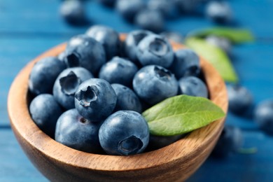 Photo of Bowl of fresh tasty blueberries on blue wooden table, closeup