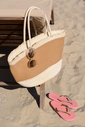 Photo of Straw bag with sunglasses and flip flops on sand . Beach accessories