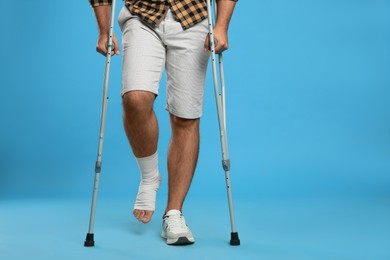 Photo of Young man with injured leg using axillary crutches on light blue background, closeup