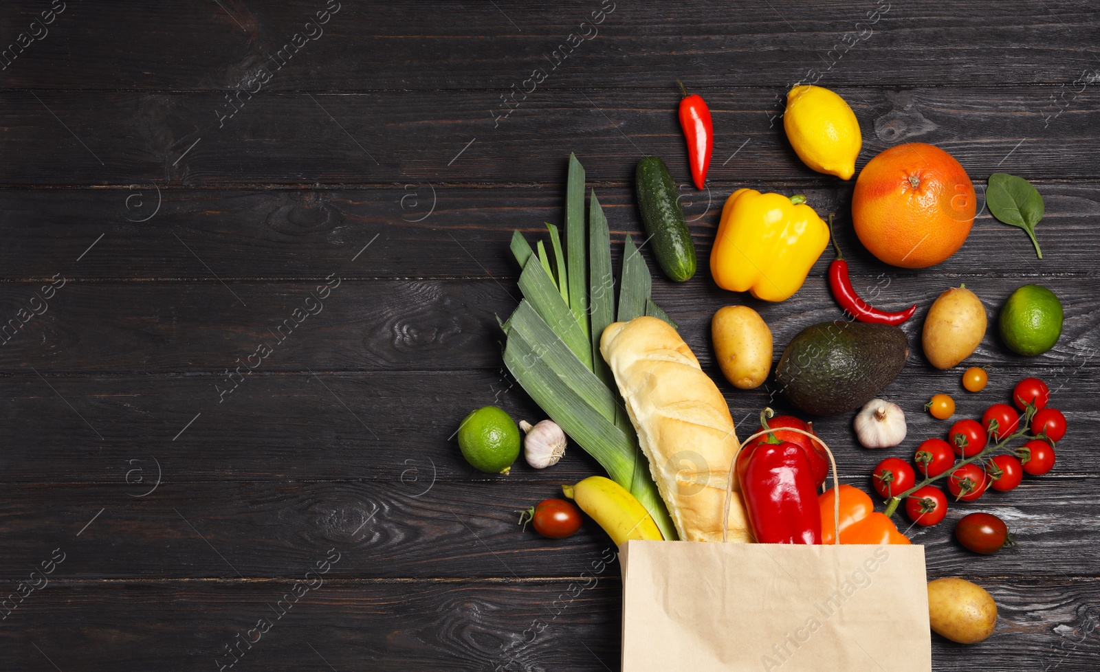 Photo of Shopping paper bag with different groceries on dark wooden background, flat lay. Space for text