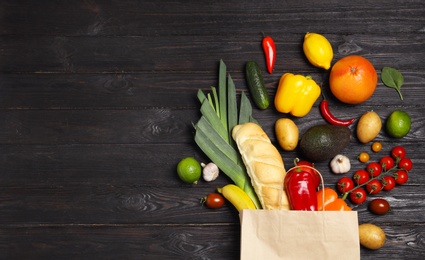 Shopping paper bag with different groceries on dark wooden background, flat lay. Space for text