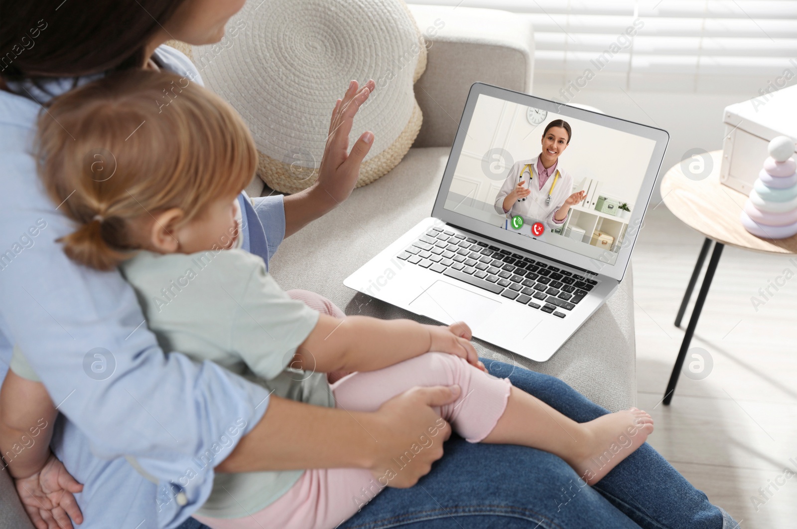 Image of Mother and daughter having online consultation with pediatrician via laptop on sofa at home